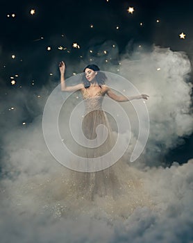 An attractive goddess stands in the clouds in a luxurious, gold, sparkling dress. Whimsical hairstyle. Against the