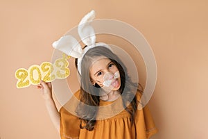 An attractive gorgeous girl in the guise of a rabbit - the symbol of the new year, holds the number 2023