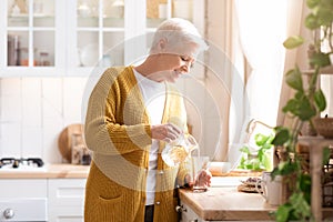 Attractive grandmother pouring water in kitchen at home