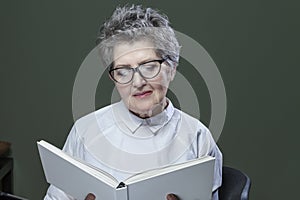 Attractive grey haired senior woman with a lovely smile relaxing at home reading a book