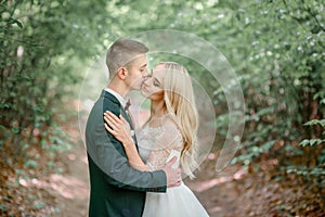 Attractive groom in green suit kisses tender bride`s cheek