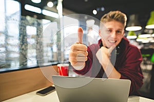 Attractive guy with a laptop in the cafe shows a thumbs up