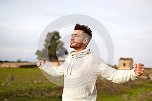 Attractive guy open his arms in the meadow.