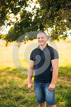 Attractive guy stand near a large green tree. Love story
