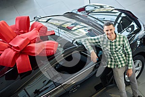 Attractive guy standing near big black auto with bow on top.