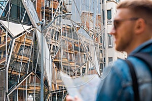 Attractive handsome man looking at map on cityscape background. European holidays. Traveller navigation concept