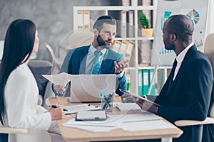 Attractive, handsome, stylish, elegant man in classic suit explaining something to his partners, three colleagues sitting in work