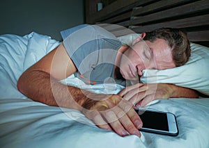 Attractive and handsome tired man on his 30s or 40s in bed sleeping peacefully and relaxed at night holding mobile phone in intern