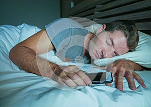 Attractive and handsome tired man on his 30s or 40s in bed sleeping peacefully and relaxed at night holding mobile phone in intern