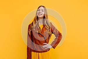 Attractive happy beautiful young woman, in a bright yellow dress and autumn jacket, poses on an  yellow background. The