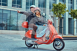 Attractive happy couple, a handsome man and female riding together on a red retro scooter in a city.