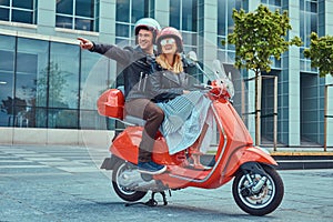 Attractive happy couple, a handsome man and female riding together on a red retro scooter in a city.