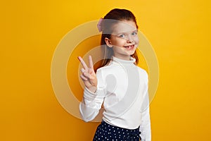 Optimistic cute girl kid showing peace gesture against bright yellow background