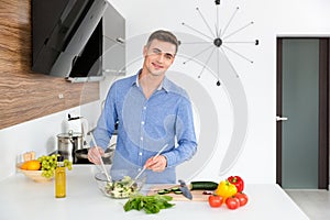 Attractive happy man making vegetarian salad on the kitchen