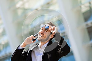 Attractive happy man talking on cell phone, raised his glasses in surprise