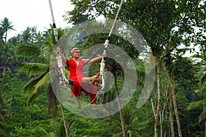 Attractive happy middle aged 40s or 50s Asian Indonesian woman with grey hair riding rainforest swing carefree swinging and