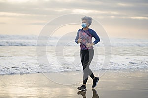 Attractive and happy middle aged woman on her 40s or 50s in face mask running doing post covid19 quarantine jogging at beautiful