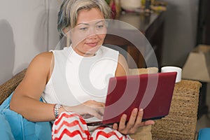 Attractive and happy middle aged woman on her 50s working on laptop computer at living room couch relaxed as independent