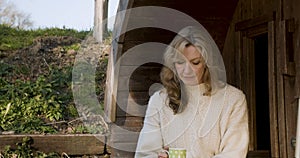 Attractive happy middle aged woman in her forties outside thoughtful, sad or depressed in sunshine with a cup of tea or coffee