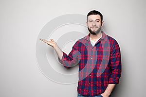 Attractive happy smiling casual young man in shirt holding copyspace on palm and showing okay gesture over gray background