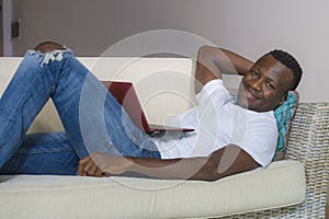 Attractive and happy successful black afro American man networking with laptop computer at living room couch smiling cheerful and