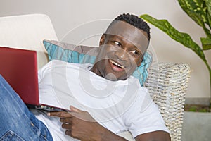 Attractive and happy successful black afro American man networking with laptop computer at living room couch smiling cheerful and