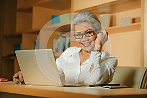 Attractive and happy successful mature Asian woman working relaxed  at laptop computer desk smiling confident in business and