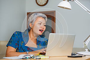 Attractive and happy successful middle aged Asian woman working at laptop computer desk smiling confident wearing elegant dress in