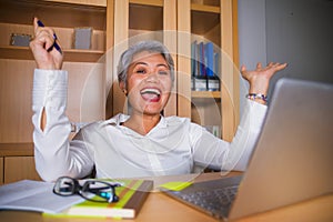 Attractive and happy successful middle aged business Asian woman working at laptop computer desk smiling confident in entrepreneur