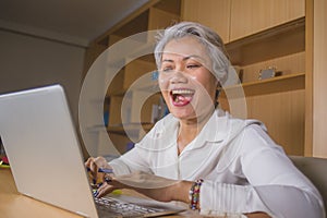 Attractive and happy successful middle aged business Asian woman working at laptop computer desk smiling confident in entrepreneur