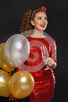 Attractive happy surprised woman with makeup and hairstyle wearing red shiny sequins dress holding party balloons, surprise