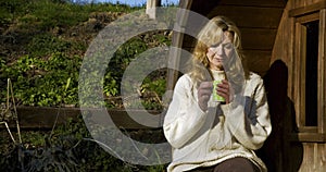 Attractive happy thoughtful middle aged woman in her forties or fifties outside drinking mug of coffee or cup of tea