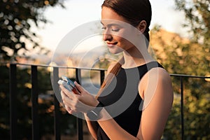 Attractive happy woman checking pulse with blood pressure monitor on finger after training in park