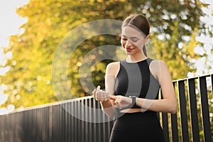 Attractive happy woman checking pulse after training in park. Space for text