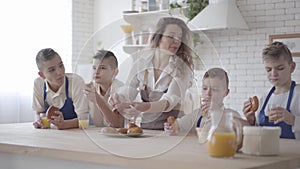 Attractive happy woman and her four teen sons eating pies and drinking orange juice in the kitcken standing at the table