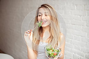 Attractive happy woman holding bowl of fresh vegetable salad in hands eating with the fork, enjoing healthy food