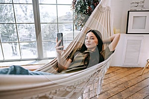 Attractive happy woman lying at the hammock, speaking on video chat, waving