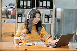 Attractive happy young Asian student studying at the college library, sitting at desk, using a laptop computer, tablet and