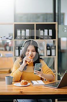 Attractive happy young Asian student studying at the college library, sitting at desk, using a laptop computer, tablet and