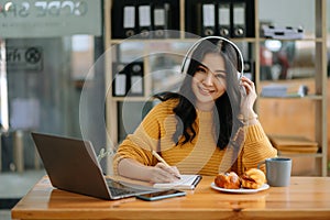 Attractive happy young Asian student studying at the college library, sitting at desk, using a laptop computer, tablet and