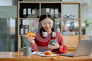 Attractive happy young Asian student studying at the college library, sitting at desk, using a laptop computer, tablet and