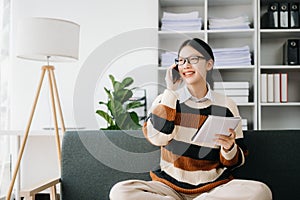 Attractive happy young Asian student studying at the college library, sitting at sofa, using a laptop computer, tablet and