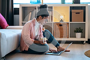 Attractive happy young entrepreneur woman working with laptop while drinking a cup of coffee sitting on the floor in the office