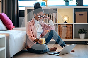 Attractive happy young entrepreneur woman working with laptop while drinking a cup of coffee sitting on the floor in the office