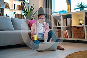 Attractive happy young entrepreneur woman working with laptop while drinking a cup of coffee sitting on the floor in the office
