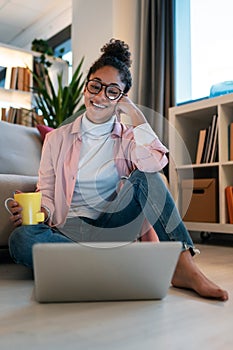 Attractive happy young entrepreneur woman working with laptop while drinking a cup of coffee sitting on the floor in the office