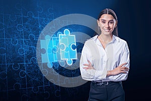 Attractive happy young european businesswoman with folded arms and abstract glowing jigsaw puzzle on blue background. Digital