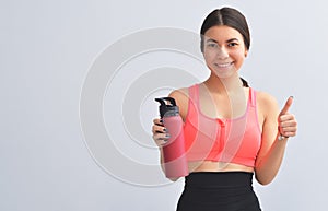 Attractive happy young fit sportswoman standing  over gray background