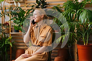 Attractive happy young woman floral shop owner sitting in own floral shop and talking on smartphone with client.