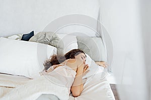 An attractive happy young woman is lying in bed with her eyes closed